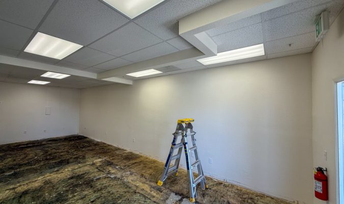 An empty commercial room during a lighting retrofit project, showing old fluorescent fixtures being replaced with energy-efficient LED panels by Mizo Electric to modernize the workspace and reduce energy costs.