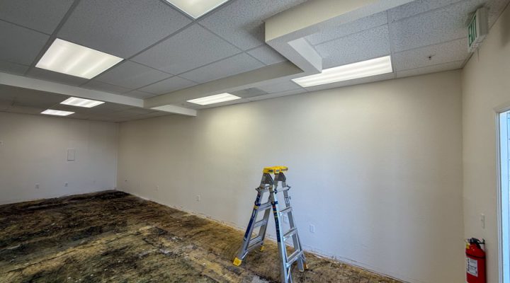 An empty commercial room during a lighting retrofit project, showing old fluorescent fixtures being replaced with energy-efficient LED panels by Mizo Electric to modernize the workspace and reduce energy costs.