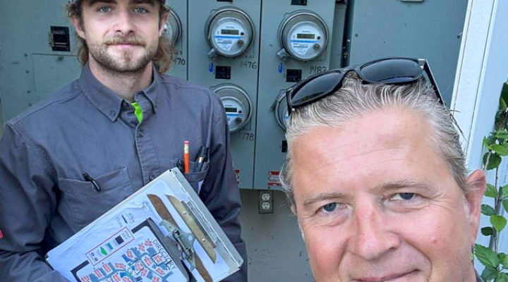 Two Mizo Electric professionals conducting a site survey in front of a multi-unit electrical meter bank, holding plans and ensuring all details are correct before starting a major service upgrade or installation in San Diego County.