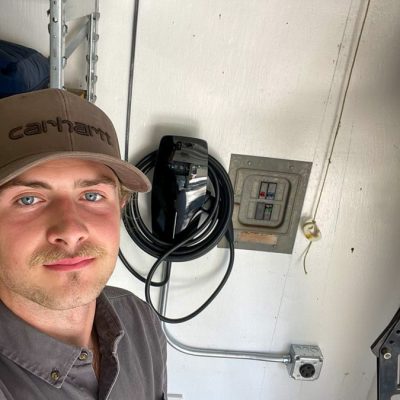 A skilled electrician stands next to a newly installed electric vehicle charger, promoting sustainable energy solutions.