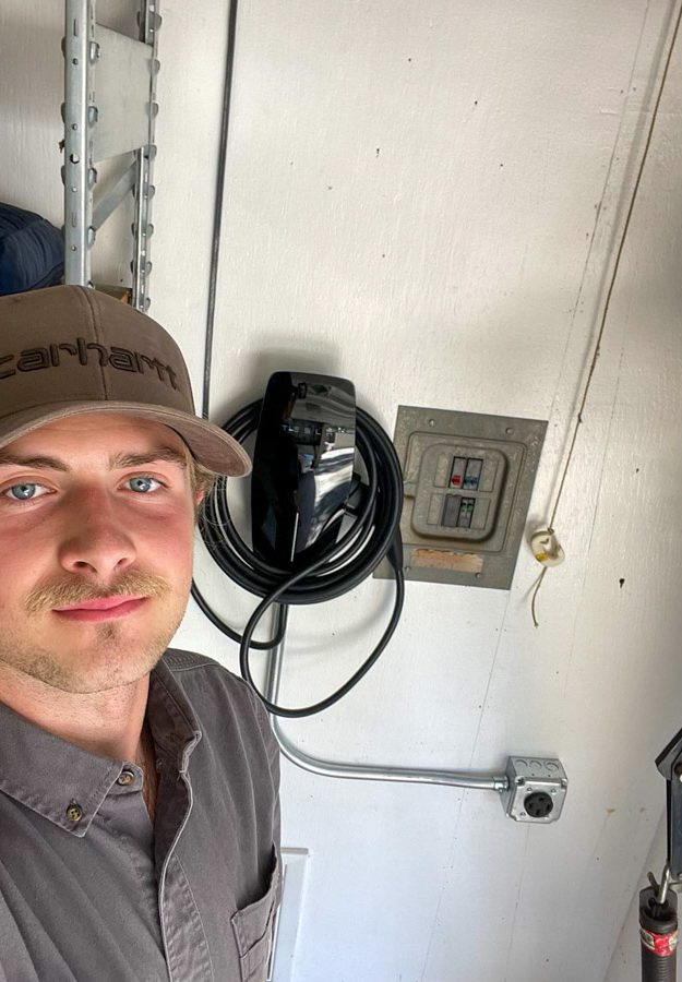 A skilled electrician stands next to a newly installed electric vehicle charger, promoting sustainable energy solutions.