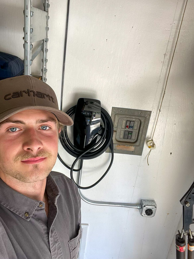 A skilled electrician stands next to a newly installed electric vehicle charger, promoting sustainable energy solutions.