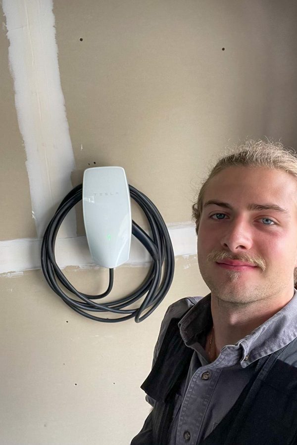 A professional electrician standing next to a newly installed Tesla EV charger, promoting eco-friendly energy solutions.