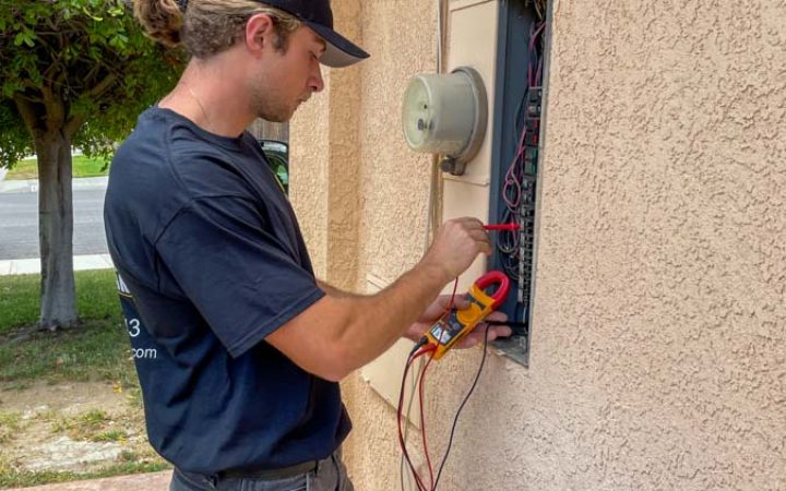 A professional electrician uses a multimeter to inspect an outdoor electrical panel, ensuring safety and functionality.
