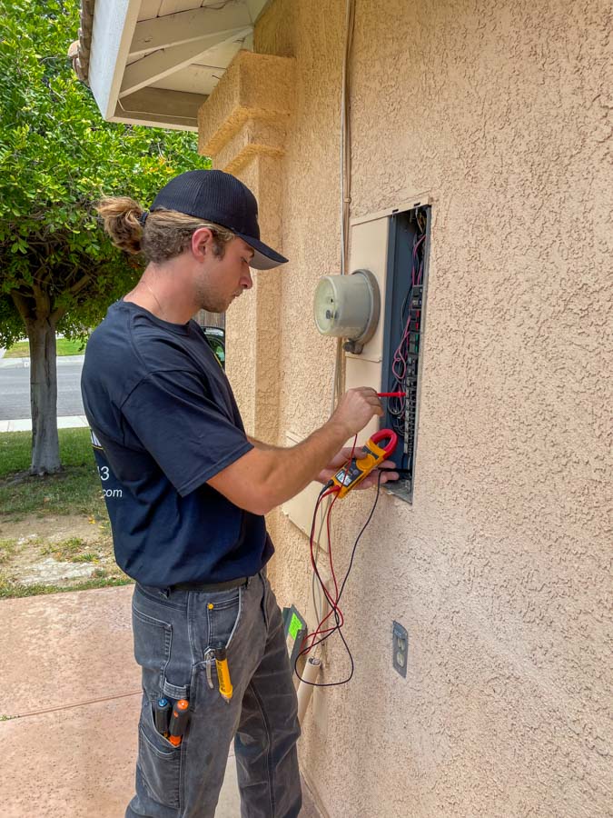 A professional electrician uses a multimeter to inspect an outdoor electrical panel, ensuring safety and functionality.