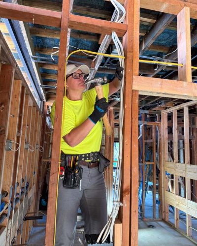 Skilled Mizo Electric technician installing electrical wiring in ceiling framework of new residential construction, providing expert electrical services in San Diego County