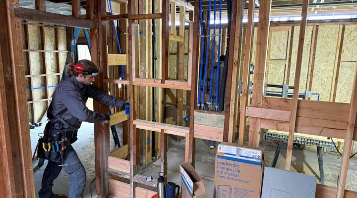 Mizo Electric professional performing electrical rough-in work during new home construction with load center panel and blue PEX plumbing visible, serving San Diego residential construction projects
